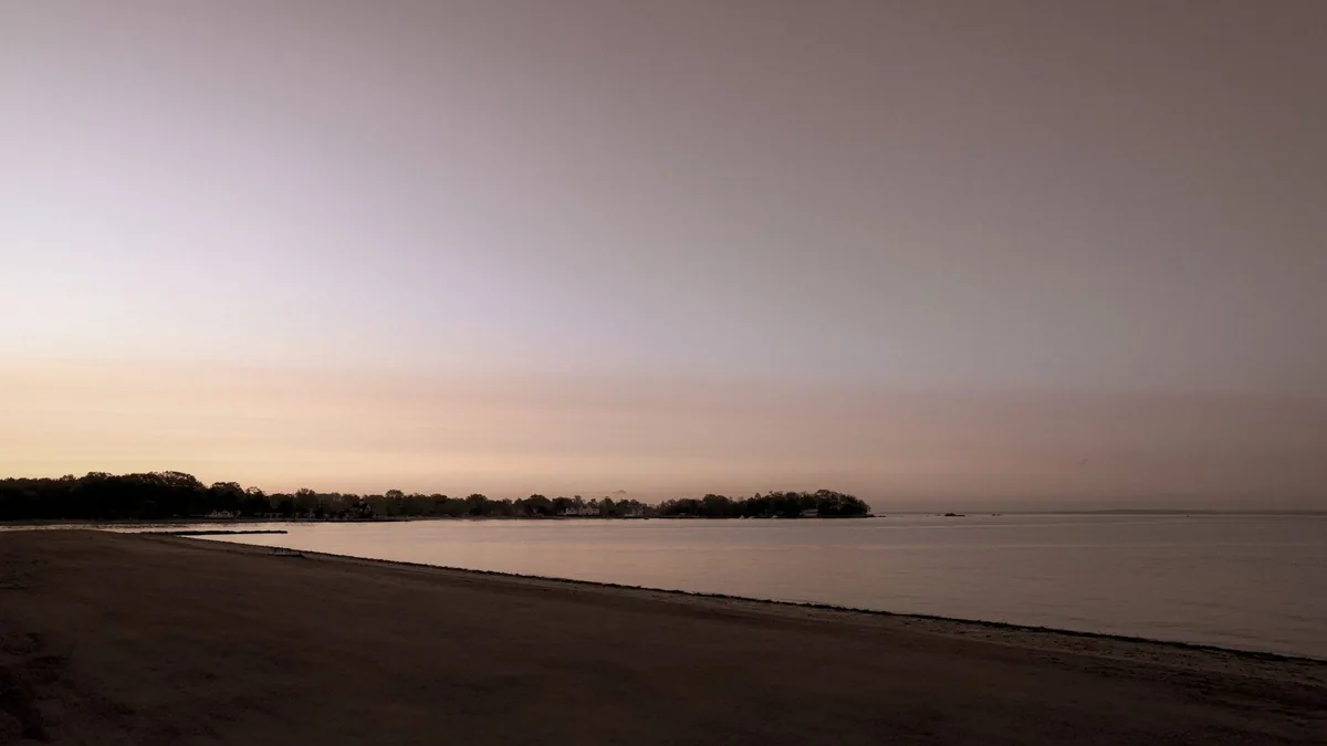 A serene sunrise over Stamford lakeshore, capturing calm water and a pastel sky.